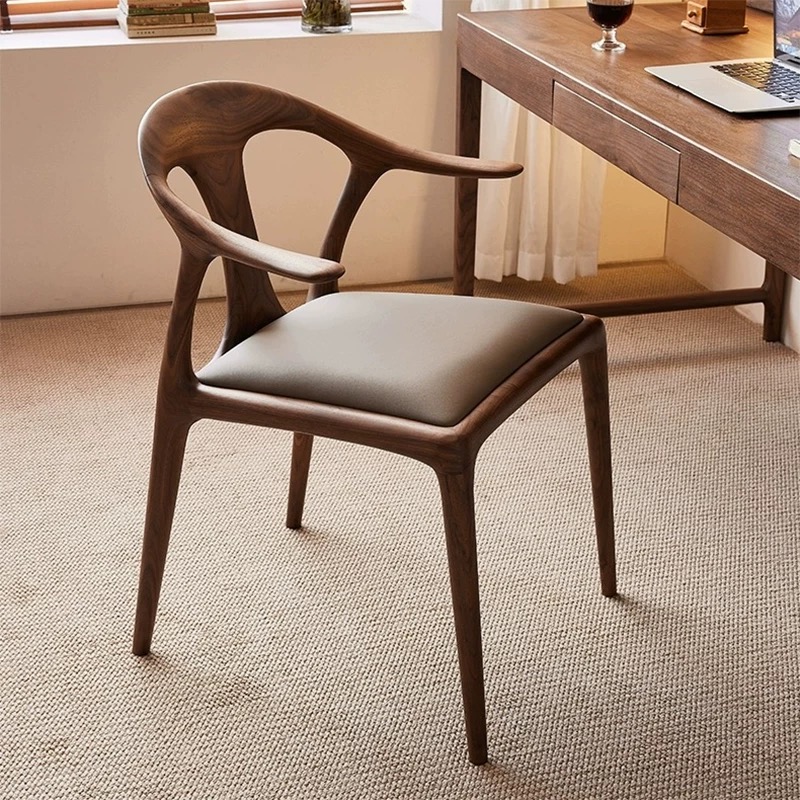 Luxury solid ash wood round back dining chair with curved armrests and leather cushion in walnut finish beside modern wooden dining table.
