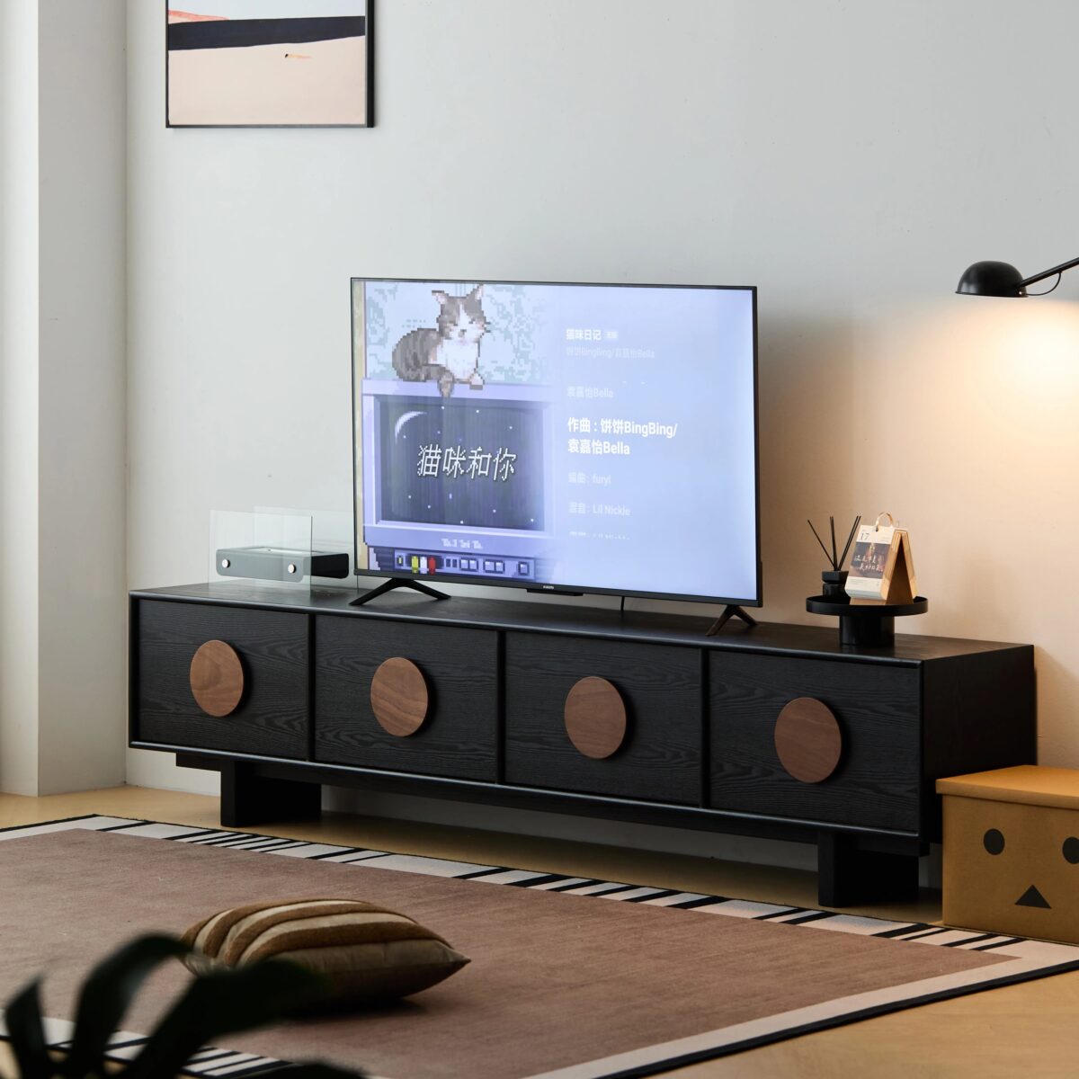 Front view of the contemporary black solid wood TV entertainment center with legs, featuring four doors adorned with distinct round walnut timber handles, supporting a flat-screen TV in a modern, minimalist living room setting.