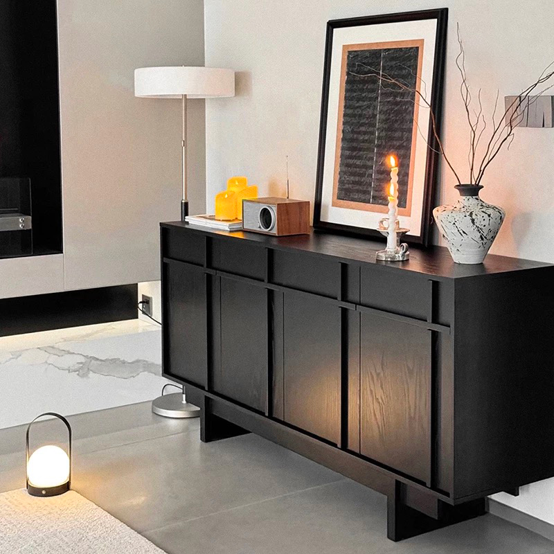 Charcoal black solid pine sideboard with carbonized wood grain texture styled with a framed art piece vase and ambient lighting in a modern dining room.