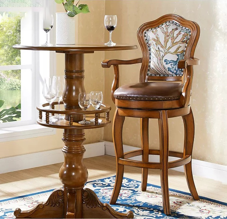 High-backed traditional luxury swivel bar stool featuring a rich brown solid wood frame, curved armrests, a plush dark brown genuine leather seat cushion with hand-hammered rivets, and a retro floral patterned fabric backrest, styled next to a wooden cabinet