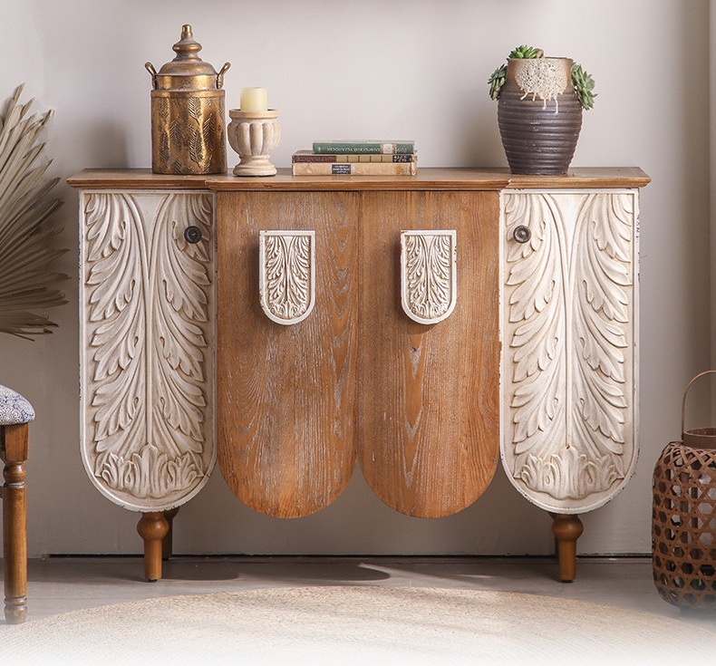 Fully assembled dual-tone rustic wood sideboard cabinet featuring hand-carved white botanical relief doors, natural fir wood grain top, and thick turned legs styled as a vintage entryway table in a bohemian-style living space.