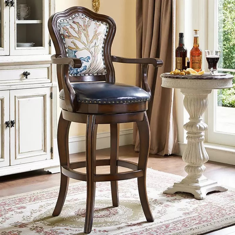 High-end Mid-Century country style counter stool with a dark black walnut finished solid wood frame, ergonomic high backrest showcasing a vintage printed jacquard pattern, hand-inlaid rivets, and a deep blue top-grain leather swivel seat cushion next to a white side table.
