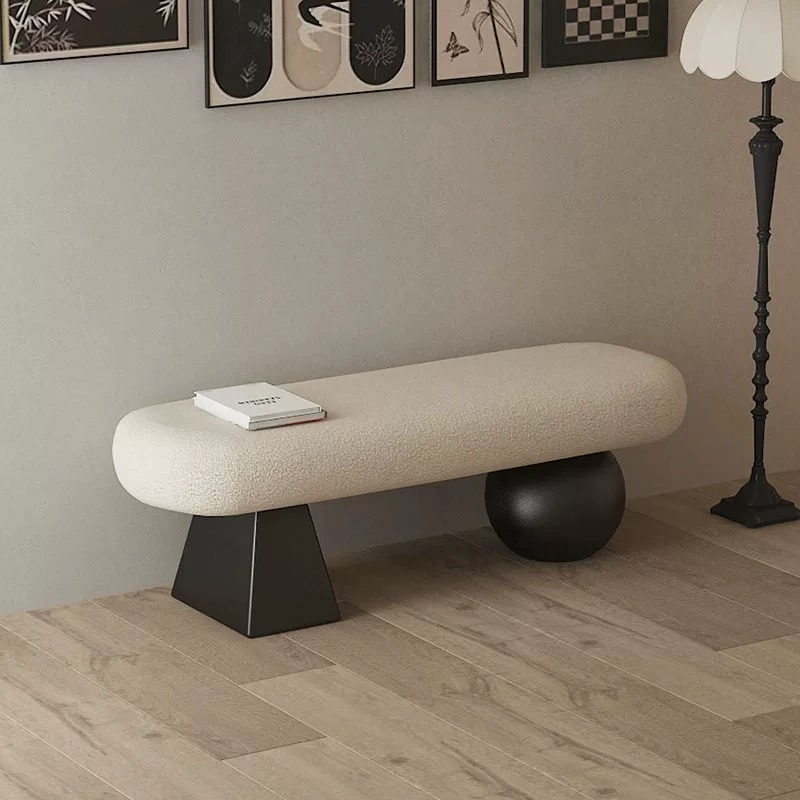 Modern luxury entryway bench with a white plush lambswool upholstered seat supported by a black geometric base and a black sculptural sphere leg on a wooden floor.