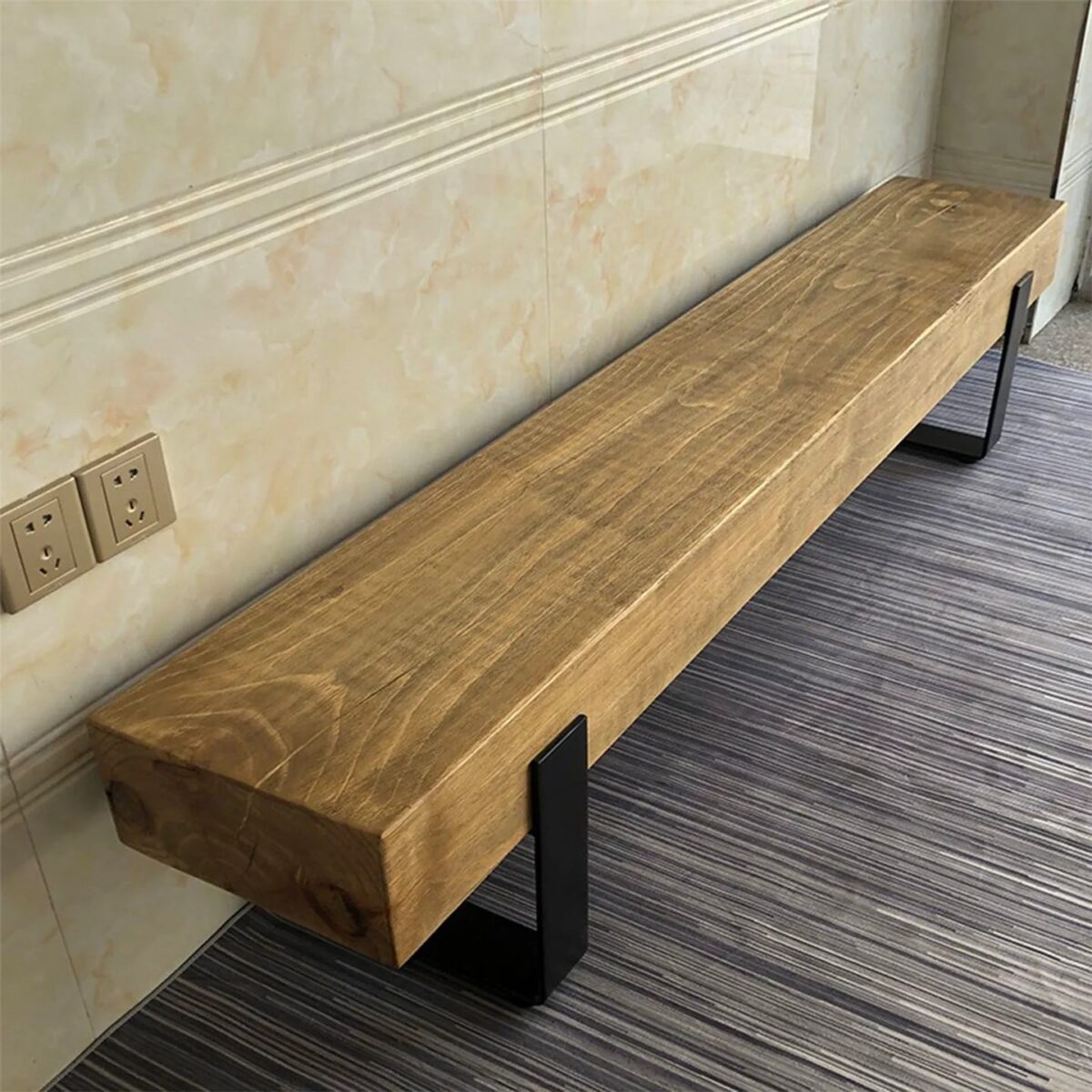 Long solid pine wood bench with natural grain finish supported by matte black metal U-shaped legs against a light wall.